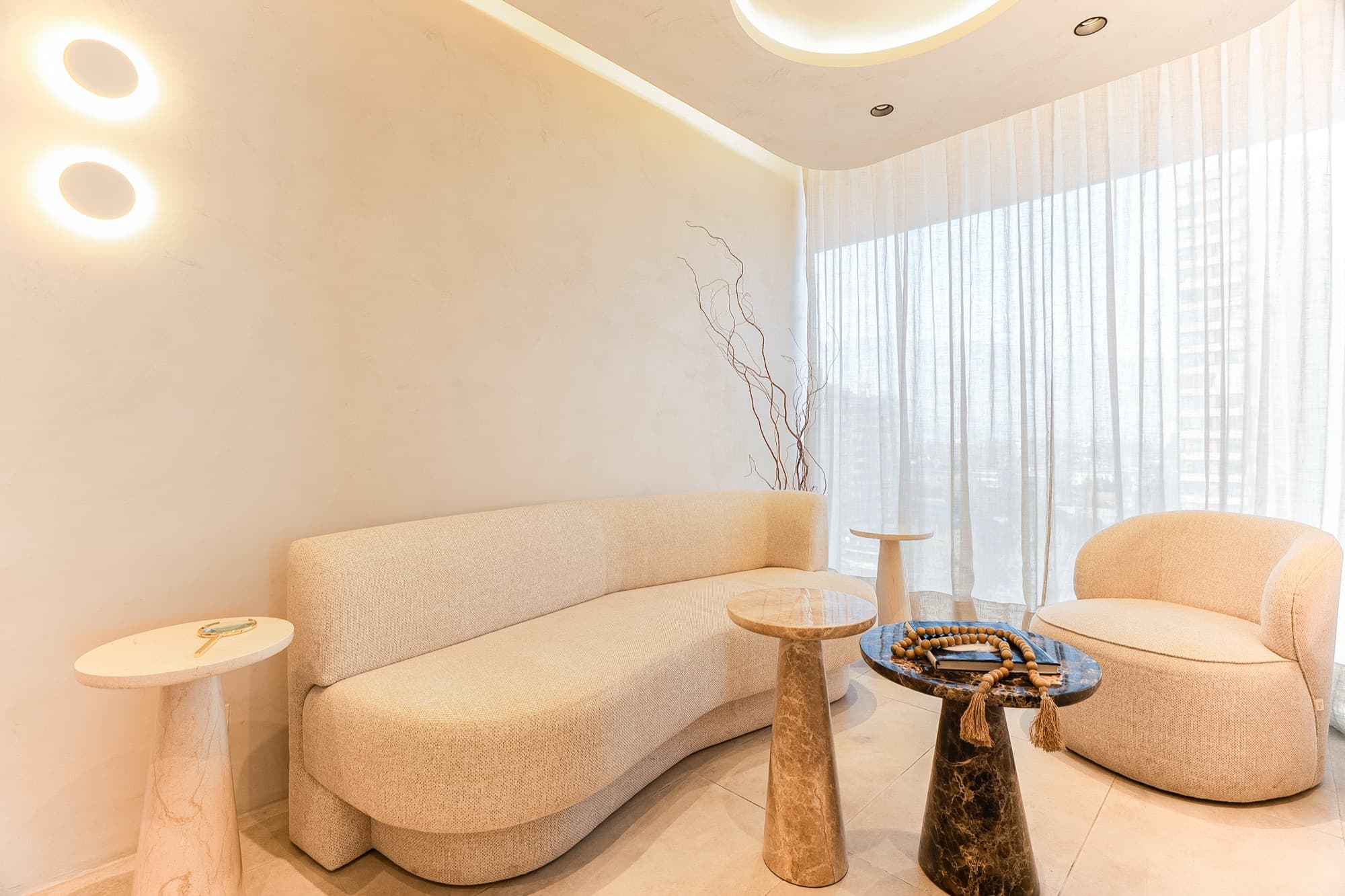 Sala de espera con sofá curvo, mesas de mármol y cortinas traslúcidas